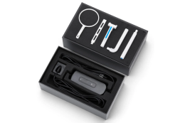 На фото показано відкриту чорну коробку: в нижній частині розміщено сам візіограф з кабелем, а у кришці знаходить набір аксесуарів. Комплект включає тримачі для сенсора, які дозволяють надійно фіксувати його та робити знімки під правильним кутом.