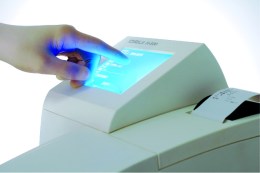 на фото зображено руку користувача, що взаємодіє з підсвіченим синім кольором дисплеєм, що підкреслює зручність та інтуїтивність інтерфейсу приладу для швидкого введення даних та запуску аналізів