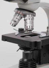 Крупний план обєктивів мікроскопа МС-20, встановлених на чотирипозиційному револьвері, та чорного механічного предметного столика. Видно маркування, а також механізм кріплення препарату